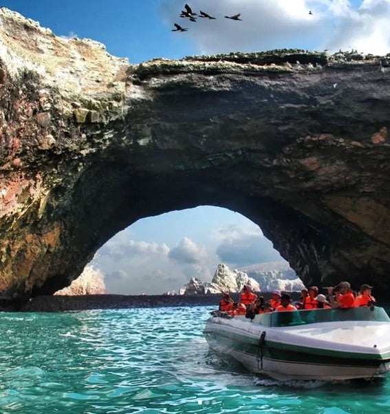 Bateau touristique passant sous une arche rocheuse aux îles Ballestas dans la réserve de Paracas au Pérou.