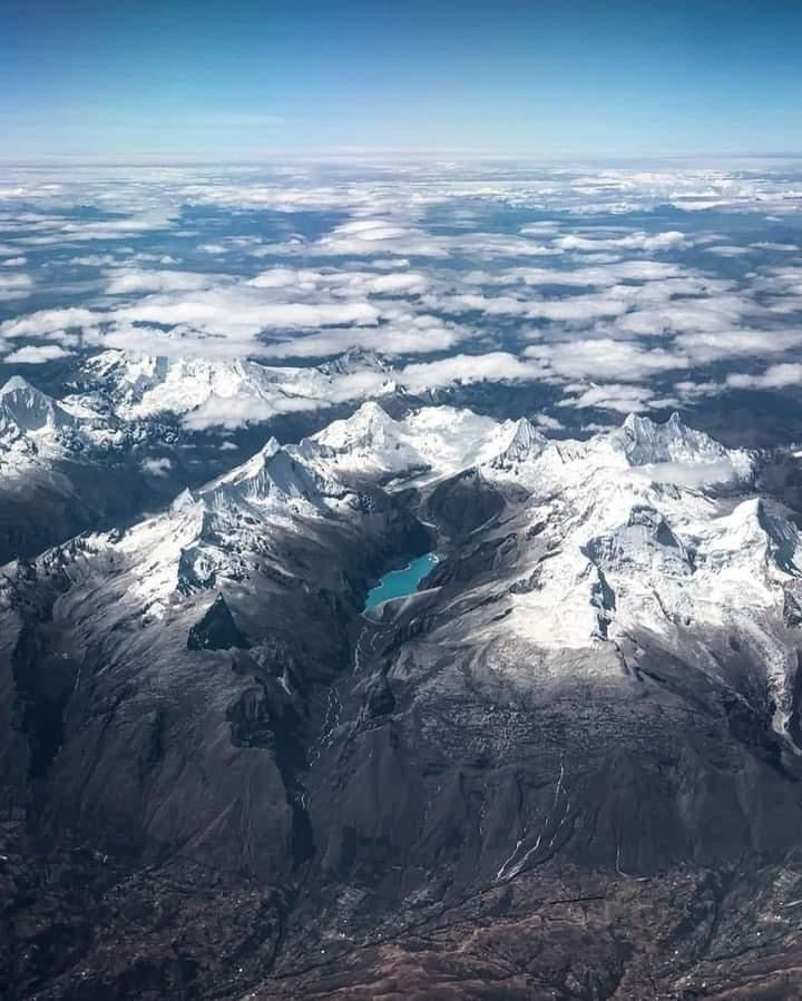 Vue aérienne de la cordillère des Andes au Pérou avec des sommets enneigés et un lac glaciaire turquoise.