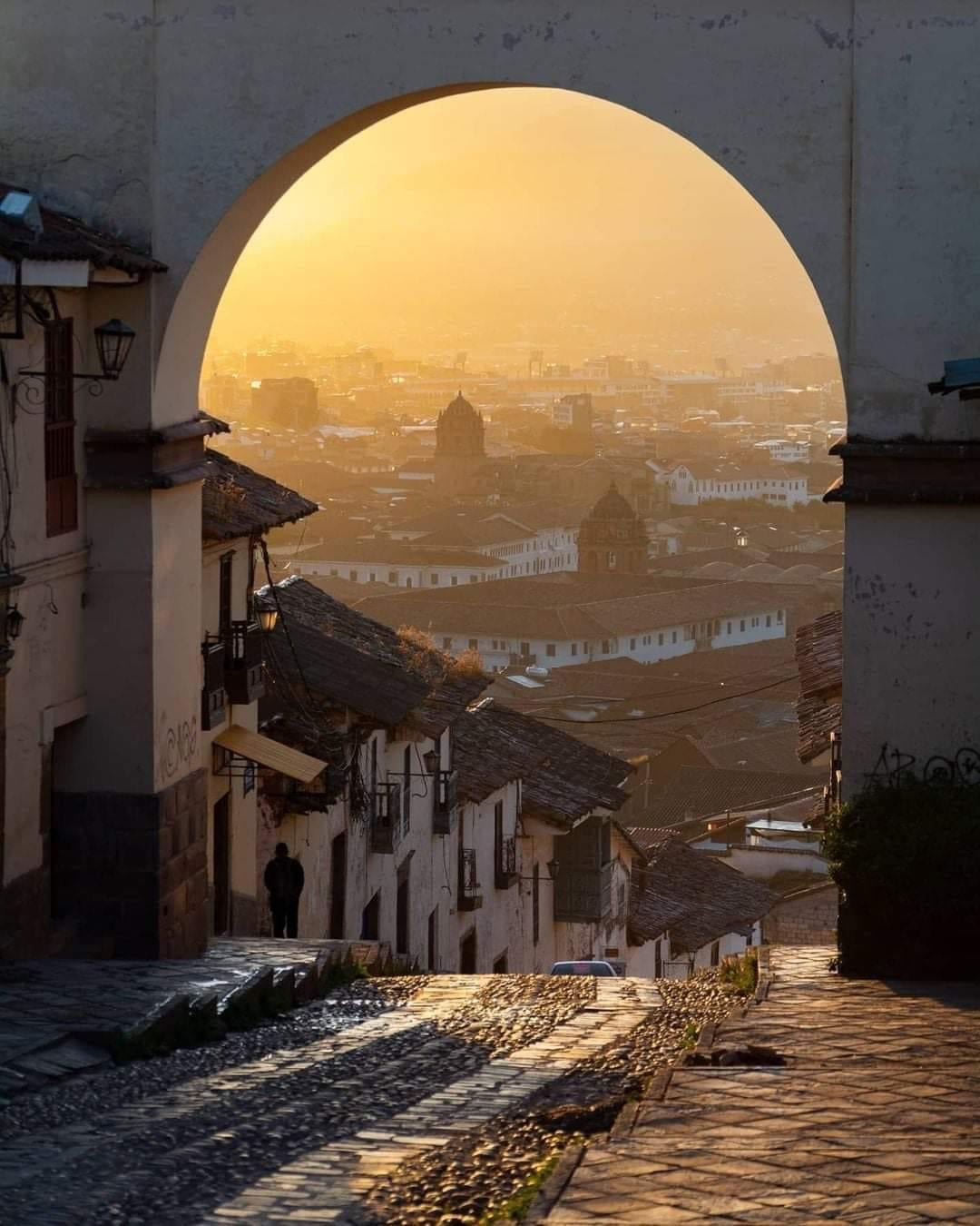 Rue pavée de Cusco avec une arche coloniale offrant une vue sur la ville au coucher du soleil au Pérou.