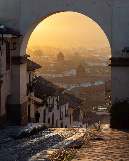 Rue pavée de Cusco avec une arche coloniale offrant une vue sur la ville au coucher du soleil au Pérou.