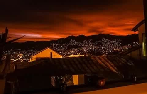 Vue nocturne de la ville de Cusco illuminée dans les Andes du Pérou sous un ciel rouge au coucher du soleil.