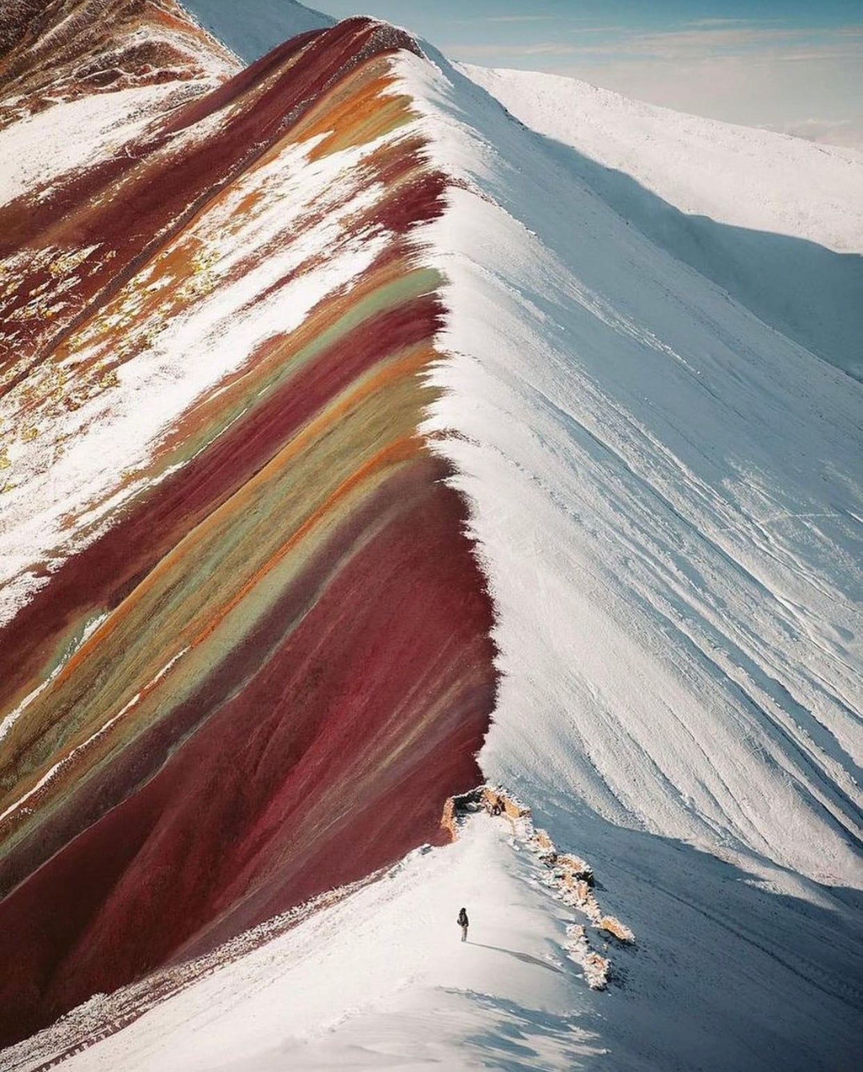 Montagne arc-en-ciel Vinicunca recouverte partiellement de neige dans les Andes au Pérou avec un randonneur sur la crête.