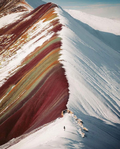 Montagne arc-en-ciel Vinicunca recouverte partiellement de neige dans les Andes au Pérou avec un randonneur sur la crête.