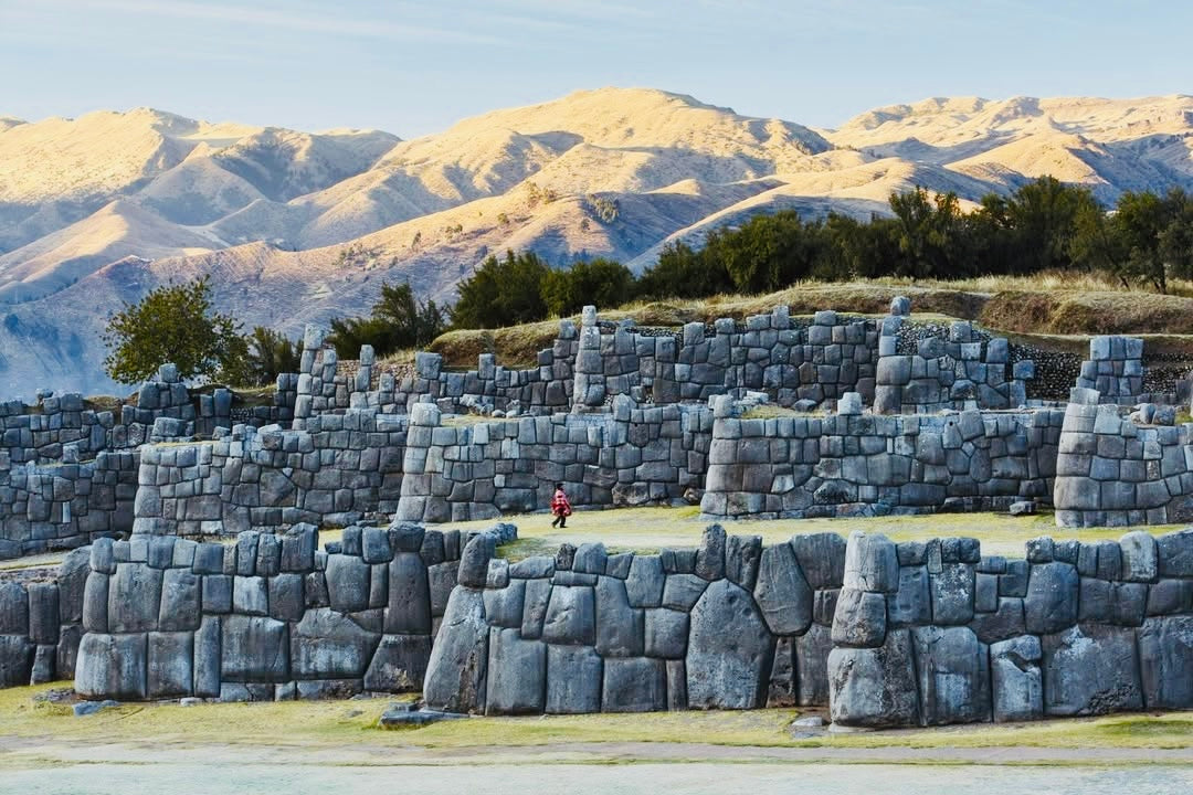 Imposants murs en pierre du site inca de Sacsayhuamán près de Cusco avec montagnes des Andes en arrière-plan.
