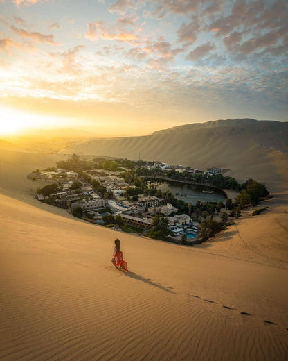 Vue de l’oasis de Huacachina entourée de grandes dunes de sable dans le désert d’Ica au Pérou au coucher du soleil.