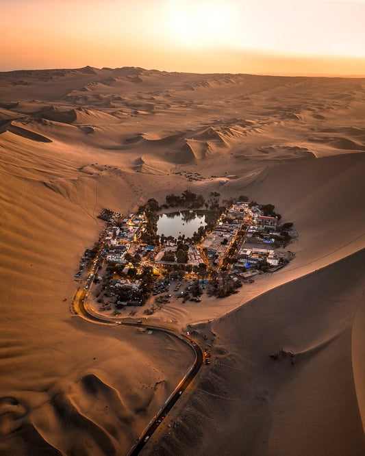 Vue aérienne de l’oasis de Huacachina entourée de dunes de sable dans le désert d’Ica au Pérou au coucher du soleil.